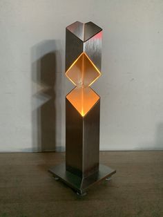 a metal sculpture with an orange light in the center on a wooden floor next to a white wall