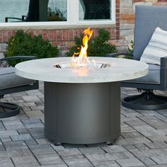 a fire pit sitting on top of a brick patio next to two chairs and a table