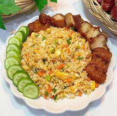 a white plate topped with rice and meat next to cucumbers on a table