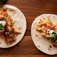 two tortillas topped with meat, cheese and sauce on a wooden table next to an avocado