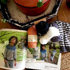 an open book with pictures of children on it and yarn in the background next to a potted plant