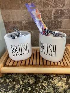 two ceramic bowls with brush and toothbrush in them sitting on a bamboo tray next to a brick wall