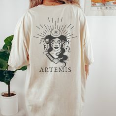 Get ready to be OBSESSED with your new Artemis Greek Mythology shirt. It's the cutest and most trendy way to combine all those important trendy light academia and greek apparel vibes! This is the perfect mythology shirt!  * Q U I C K * F A C T S * ✺  All shirts are UNISEX ✺  100%  ringspun cotton (fiber content may vary for different colors) ✺  Soft-washed, garment-dyed fabric brings extra coziness ✺  Wash and dry normally (on cool for best results) ✺  Sewn-in twill label * S I Z I N G * ✺ For an oversized fit, select two or three sizes up from your normal size ✺ Model is wearing size L  ✺ Sizing runs true to size ✺ Relaxed fit ✺ Most women find their typical size works best, since they are meant to fit a touch loose ✺ See Size guide and fit in images          * S H I P P I N G * T I M E S Relaxed Fit Graphic Print Shirt In Bookish Style, Relaxed Fit Graphic Print Shirt With Bookish Style, Bookish Cotton Shirt With Graphic Print, Artistic Relaxed Fit Shirt With Screen Print, Artemis Greek Mythology, Goddess Mythology, Greek Letter Shirts, Artemis Goddess, Poet Shirt