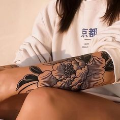 a woman with a flower tattoo on her arm and leg is sitting in front of a white wall