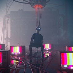 a man sitting on a chair in front of several televisions with colored lights behind him