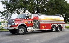 a red and yellow fire truck driving down the street with trees in the back ground