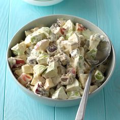 a bowl filled with salad sitting on top of a blue table next to a spoon