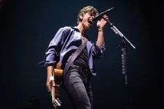 a man singing into a microphone while holding an acoustic guitar in his hand on stage