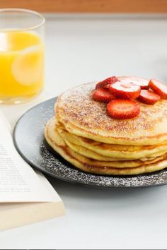 a stack of pancakes with strawberries on top next to a glass of orange juice