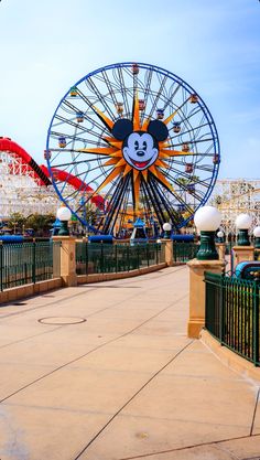 an amusement park with a ferris wheel and mickey mouse face on the front, surrounded by other rides