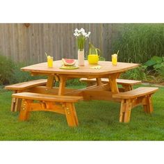 a wooden picnic table with two benches in the grass next to a fence and flowers