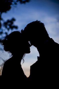 the silhouette of a man and woman kissing in front of a blue sky with clouds