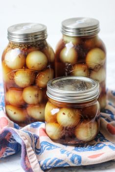 three jars filled with pickled onions on top of a blue and white cloth next to a