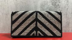 "This beautiful clutch is a must-have, perfect as a gift or an accessory for holiday outings.  The entire front of the clutch is covered with silver and black seed beads, creating a Chevron design across the front- adding glamour and shine, with elegance.  The back is covered with black seed beads and the inside is made of fabric with one pocket inside. Features a chain that converts into a shoulder purse. Hand-sewn seed beads. Measures: 5\"X9\"; with chain 14\" Snap button closure One inside sl Silver Beaded Clutch For Gift, Silver Beaded Clutch For Formal Occasions, Formal Silver Beaded Clutch, Chain Purse, Event Gifts, Black Seed, Chevron Design, Purse Bag, Shoulder Purse