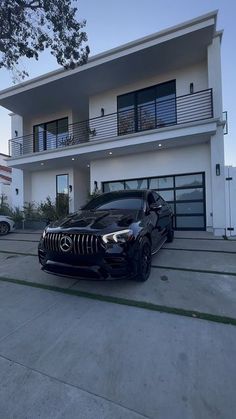 a black car is parked in front of a white house with two balconies