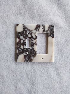 a marble light switch plate cover with black and white designs on the bottom, sitting on a gray surface