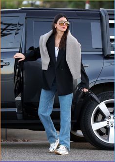 a woman is standing in front of a black suv with her luggage and wearing sunglasses