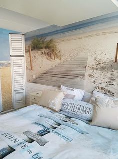 there is a bed with many pillows on it and a wall mural behind it that has a boardwalk leading to the beach