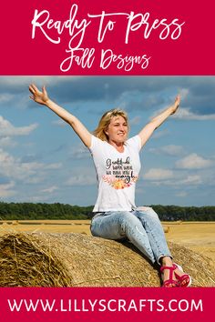 a woman sitting on top of a hay bale with her arms in the air