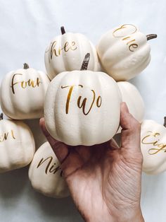 white pumpkins with gold writing on them are being held up by someone's hand