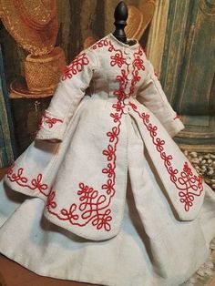 the doll is wearing a white dress with red embroidery