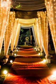 an outdoor wedding ceremony with white drapes and lights on the aisle leading into the venue