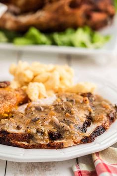 a white plate topped with meat covered in gravy next to a pile of potatoes