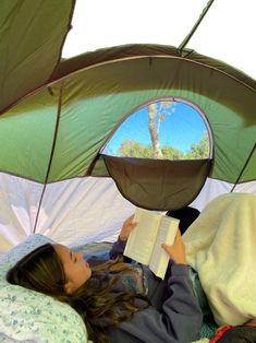 a woman laying in bed under an umbrella reading a book with her head on the pillow