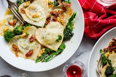 two white plates with ravioli, spinach and cheese on them next to wine glasses