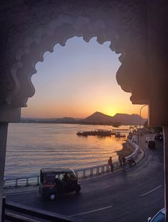 the sun is setting over some water and cars