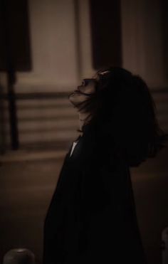 a woman standing in the dark with her hair blowing back and looking up at something