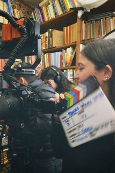 a woman holding a video camera in front of a book shelf with books on it