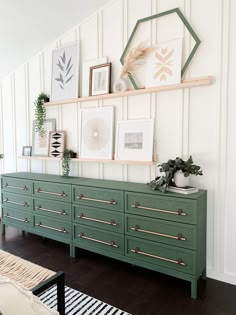 a green dresser in a white room with pictures and plants on the wall above it