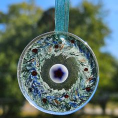 a glass ornament hanging from a blue ribbon with trees in the back ground