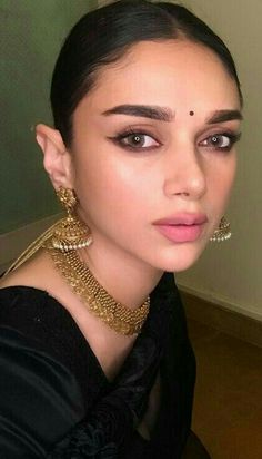 a woman with dark hair and gold jewelry on her neck is looking at the camera