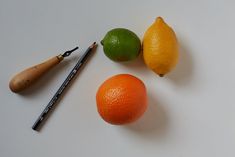 three lemons, two oranges and a pen on a white surface with a pencil