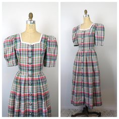 "Vintage cotton plaid dress with short puff sleeves. Bodice has princess seams. Full pleated skirt with side pockets. Buttons all the way down the front with large pewter buttons. There's even an extra button sewn to the inside of the skirt. I believe this dress was made in Germany because of the writing on the fabric content tag. Excellent vintage condition.  Clean and ready to wear. Measurements: Shoulders: 15.5\" Bust: 35\" Waist: 30\" Hips: open Shoulder to hem length: 47.5\" Shoulder to wai Vintage Gingham Plaid Dress With Short Sleeves, Plaid Cotton A-line Dress, Retro Cotton Plaid Dress, Vintage A-line Plaid Dress, Vintage Plaid Dress With Button Closure, Princess Seam, Plaid Dress, Sewing A Button, Vintage Cotton