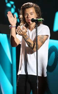 a man with long hair and tattoos on his arm holding a microphone in front of him