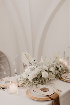 the table is set with white flowers, candles and place settings for an elegant dinner