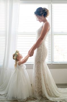 a mother and her daughter standing in front of a window holding each other's hands