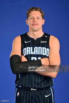 a basketball player poses for a photo in front of a blue background with his arms crossed