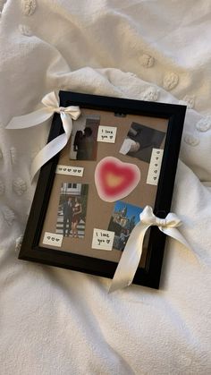 a photo frame with pictures and ribbons attached to it on a white sheeted bed