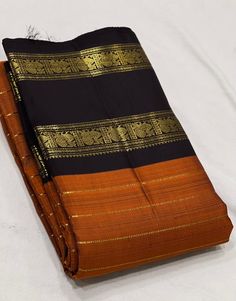 an orange and black saree laying on top of a white bed sheet covered in gold thread