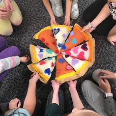 several people sitting on the floor around a large pizza shaped like a pie with hearts