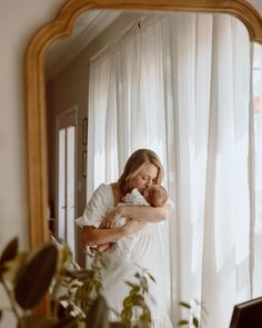 a woman holding a baby in her arms while looking at the camera through a mirror