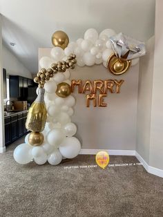 a balloon arch that says marry me in gold, white and silver balloons hanging from the ceiling