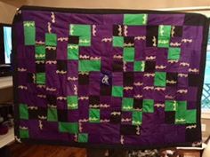 a purple and green quilt hanging from a wall