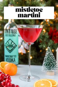 a red drink in a glass next to some oranges and christmas tree with the words mistleoe martini on it