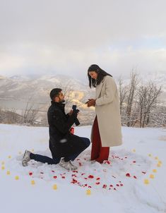 a man kneeling down next to a woman on top of a snow covered field with rose petals