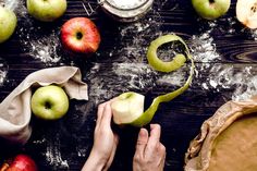 someone is peeling an apple into pieces on a table with other apples and pie ingredients